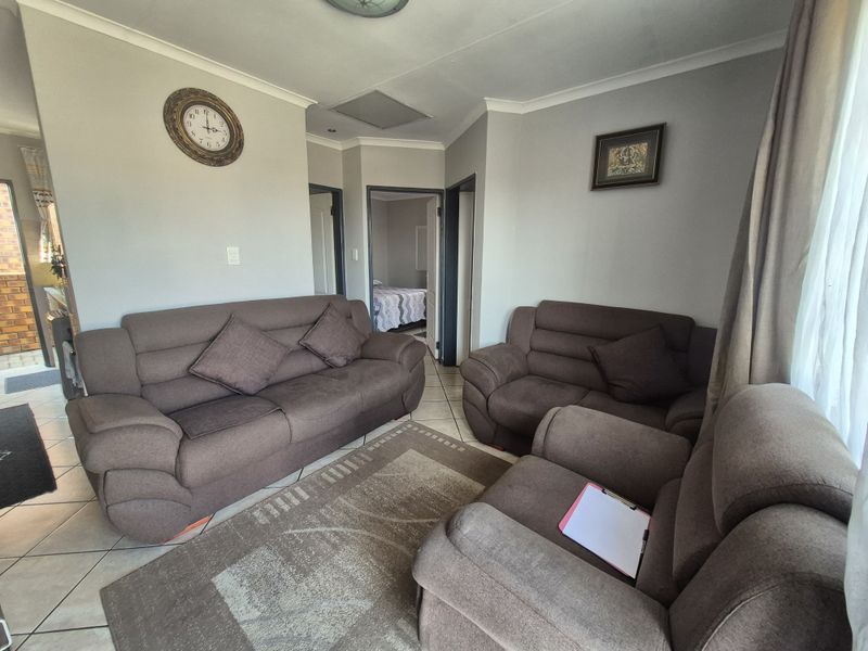 A comfortable living room featuring tiled flooring, neutral wall tones, and access to adjacent rooms.