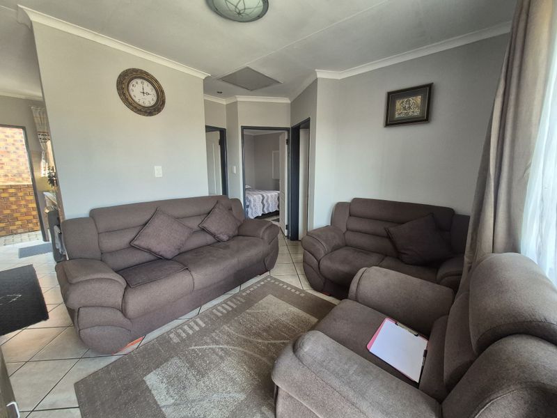 A comfortable living room featuring tiled flooring, neutral wall tones, and direct access to adjacent rooms and an outdoor area.