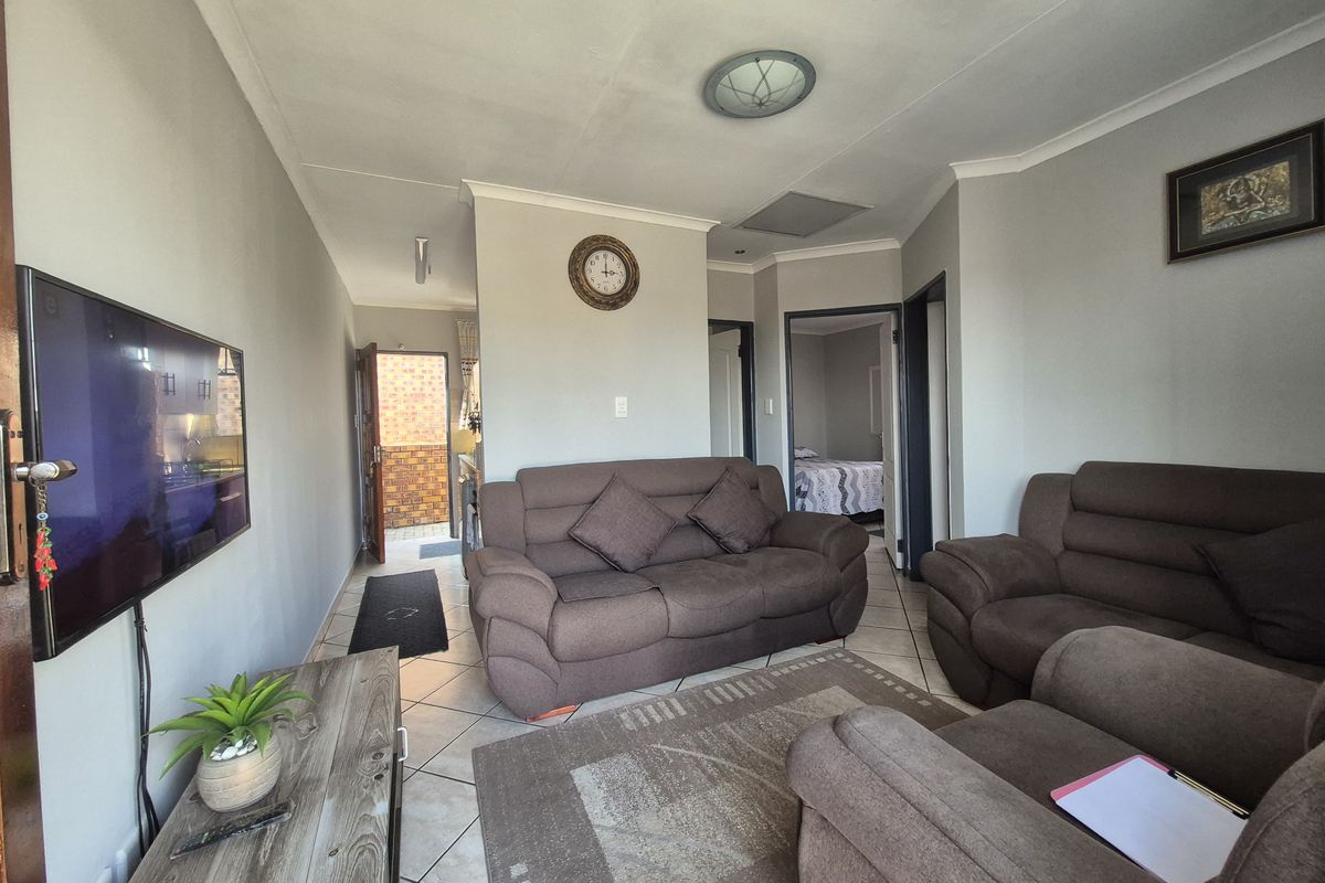 A living room featuring tiled flooring, neutral wall tones, and access to adjacent rooms and an exterior entrance.
