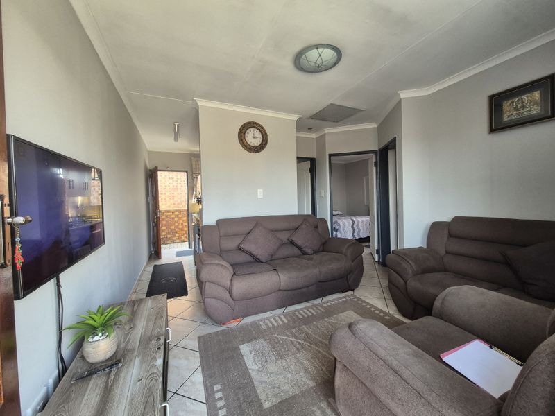 A living room featuring tiled flooring, neutral wall tones, and access to adjacent rooms and an exterior entrance.