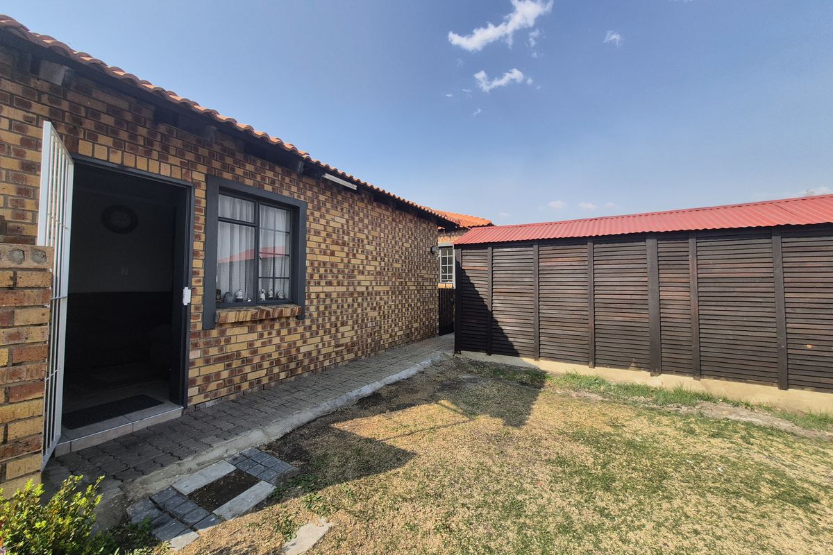 A view of the rear exterior featuring face-brick walling, a paved walkway, and a detached wooden storage structure set within a garden area.