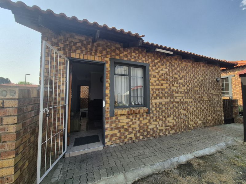 Exterior view of a face-brick residential unit featuring a security gate, tiled roof, and paved walkway entrance.