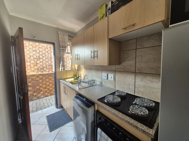 A functional kitchen featuring light wood cabinetry, a built-in electric hob, tiled backsplash, and direct access to an exterior paved area.