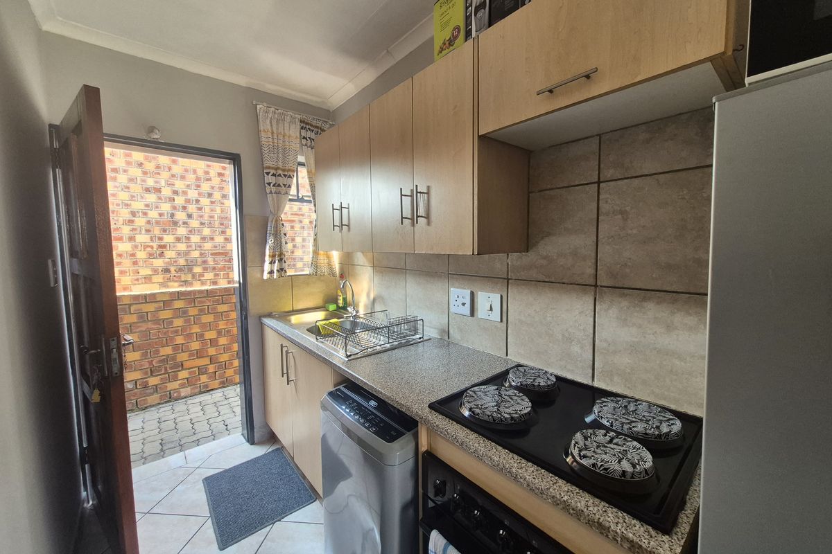 A functional kitchen featuring light wood cabinetry, a built-in electric hob, tiled backsplash, and direct access to an exterior paved area.