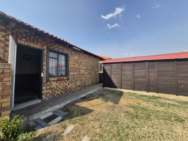 A view of the rear exterior featuring face-brick walling, a paved walkway, and a detached wooden storage structure set within a garden area.