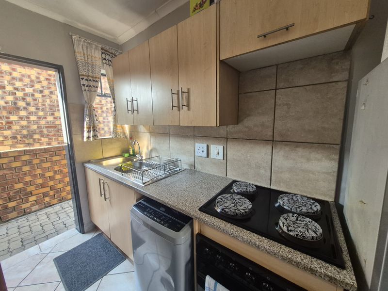 Compact kitchen featuring light wood cabinetry, stone-look laminate countertops, a built-in electric hob, and direct access to an exterior paved area.