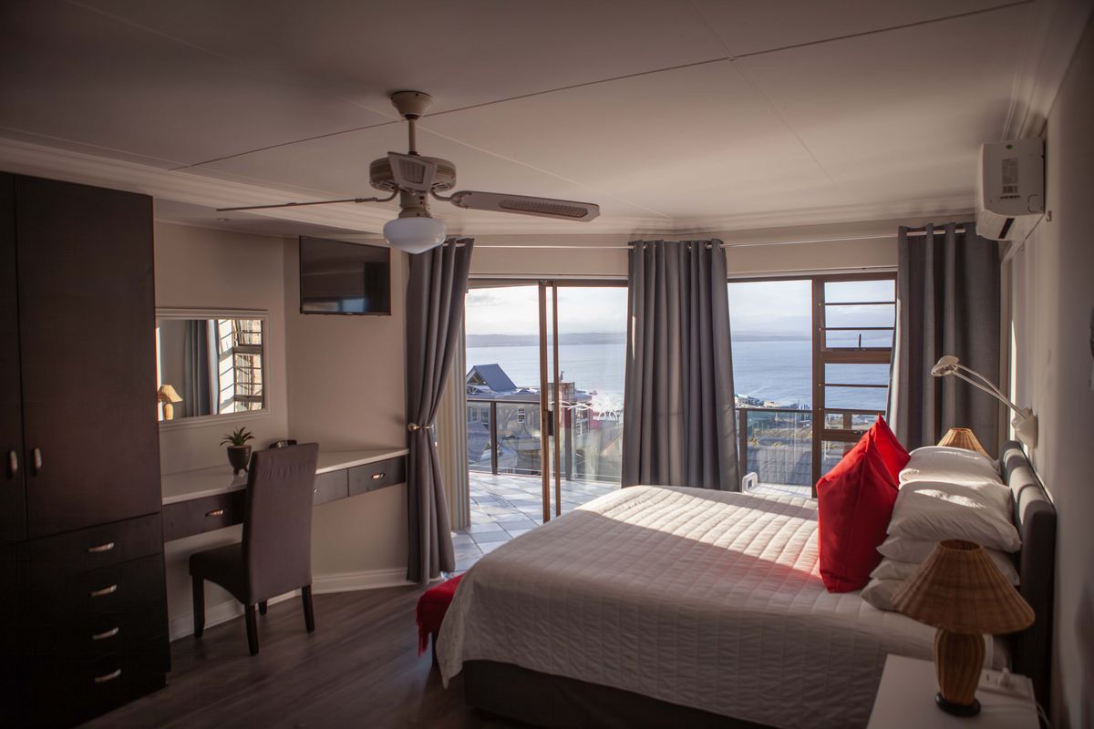 A well-appointed bedroom featuring a built-in vanity, ceiling fan, and sliding glass doors that open to a balcony with scenic ocean views.