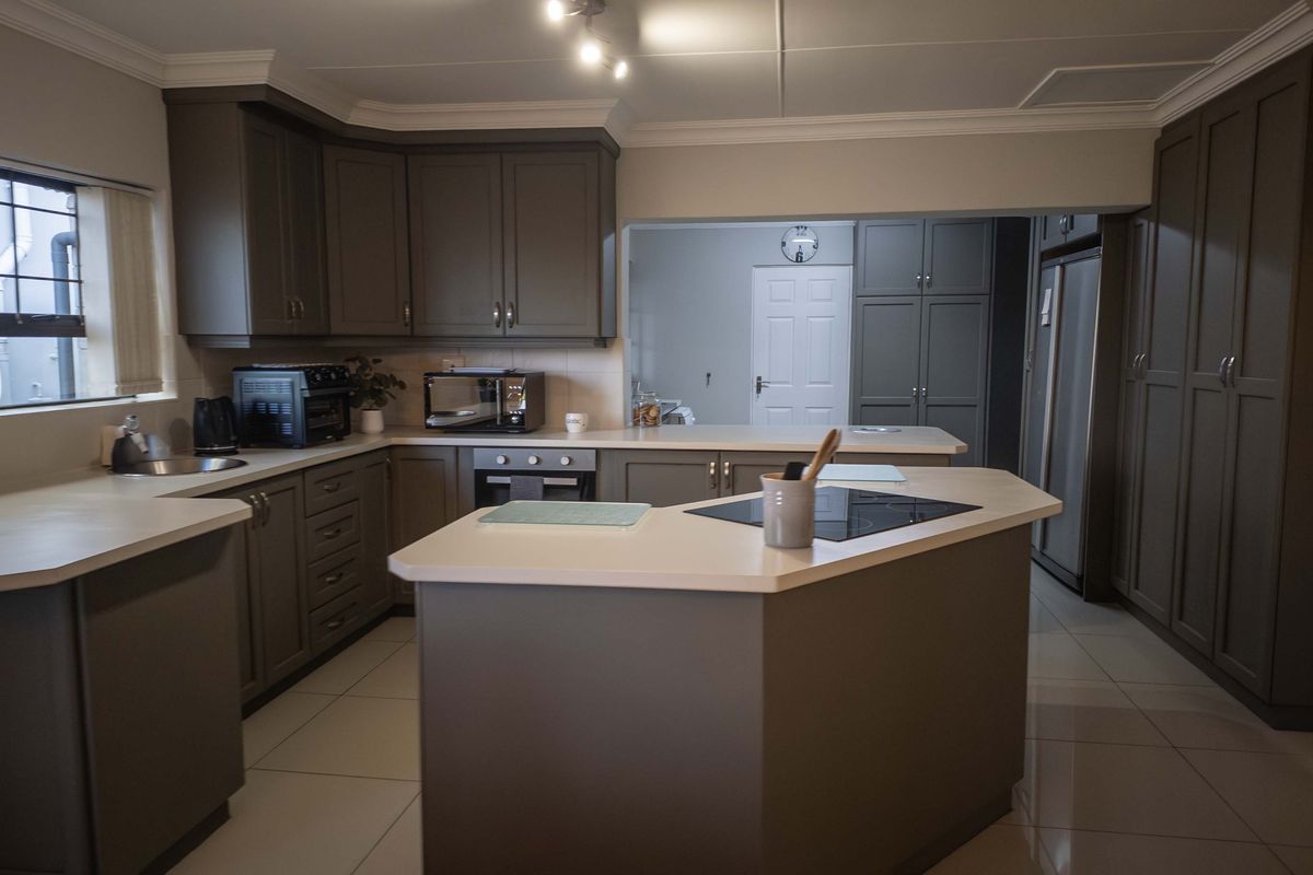 Modern kitchen featuring dark grey cabinetry, a central island with a built-in hob, light countertops, and tiled flooring.