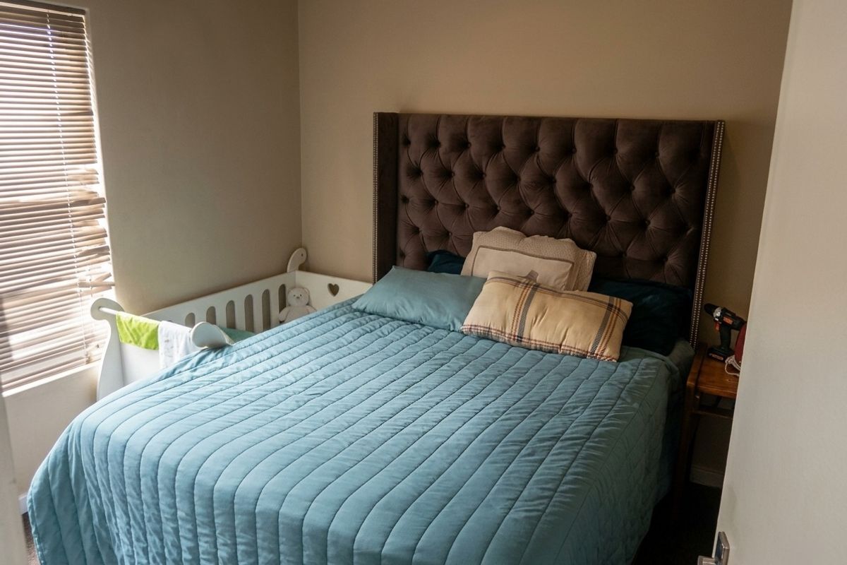 A functional bedroom featuring neutral wall tones and venetian blinds, providing a comfortable space for rest.
