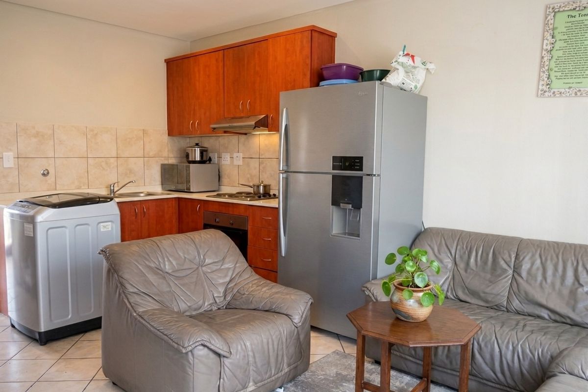 Open-plan kitchen area featuring wooden cabinetry, tiled backsplash, and integrated cooking appliances, seamlessly connected to the living space.