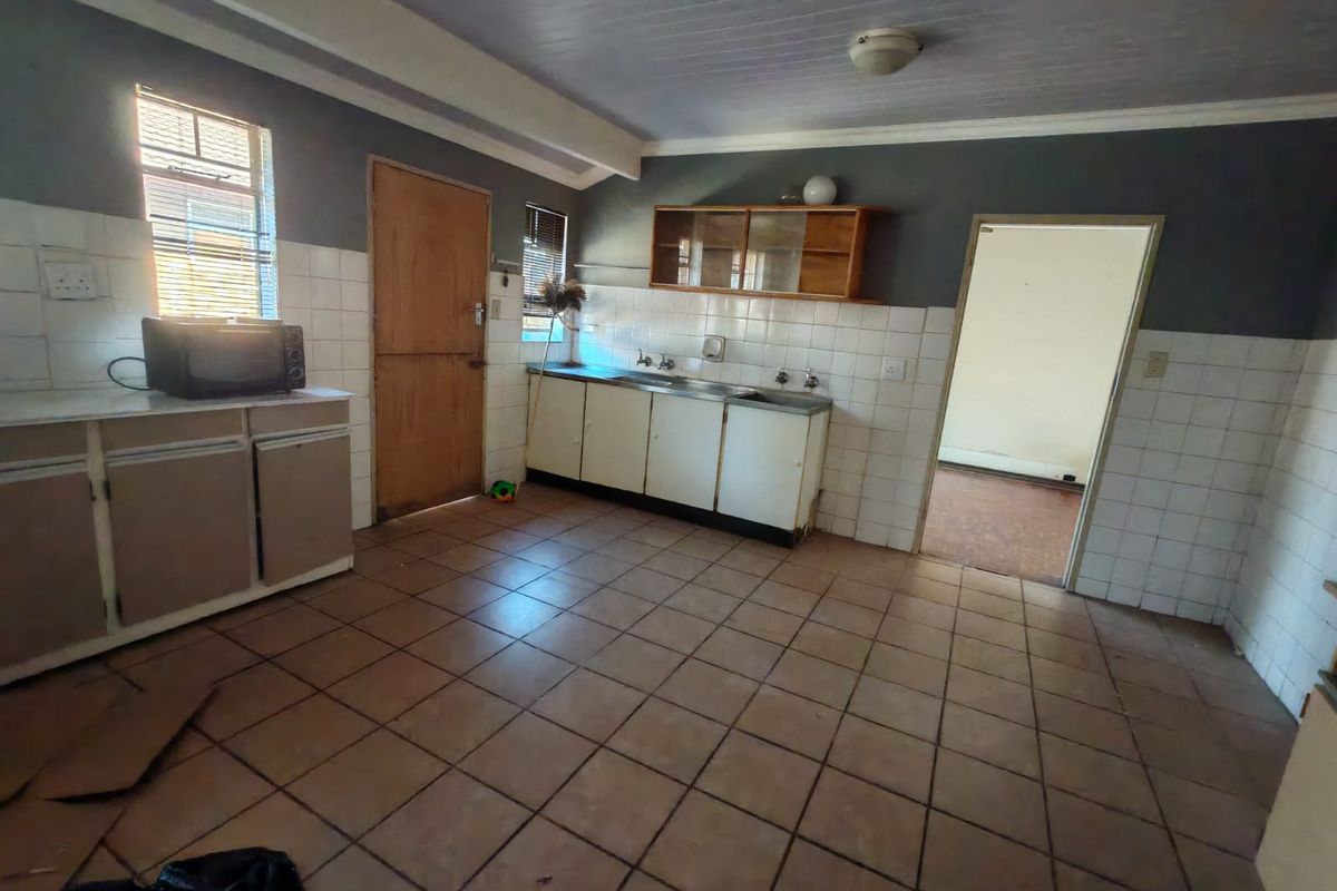 A dated kitchen featuring tiled flooring, built-in cabinetry, and a stainless steel sink, offering significant potential for renovation and modernization.