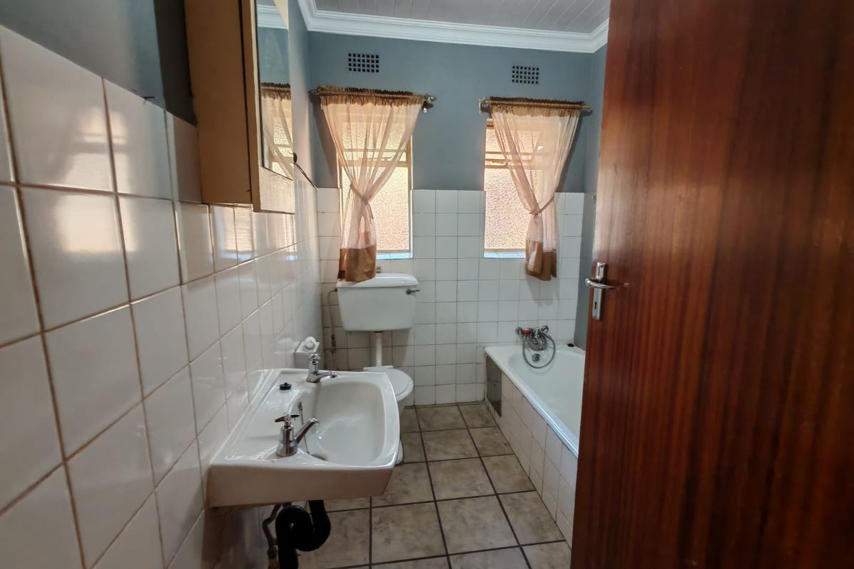 A dated bathroom featuring a pedestal basin, toilet with high-level cistern, and a built-in bathtub with tiled finishes.