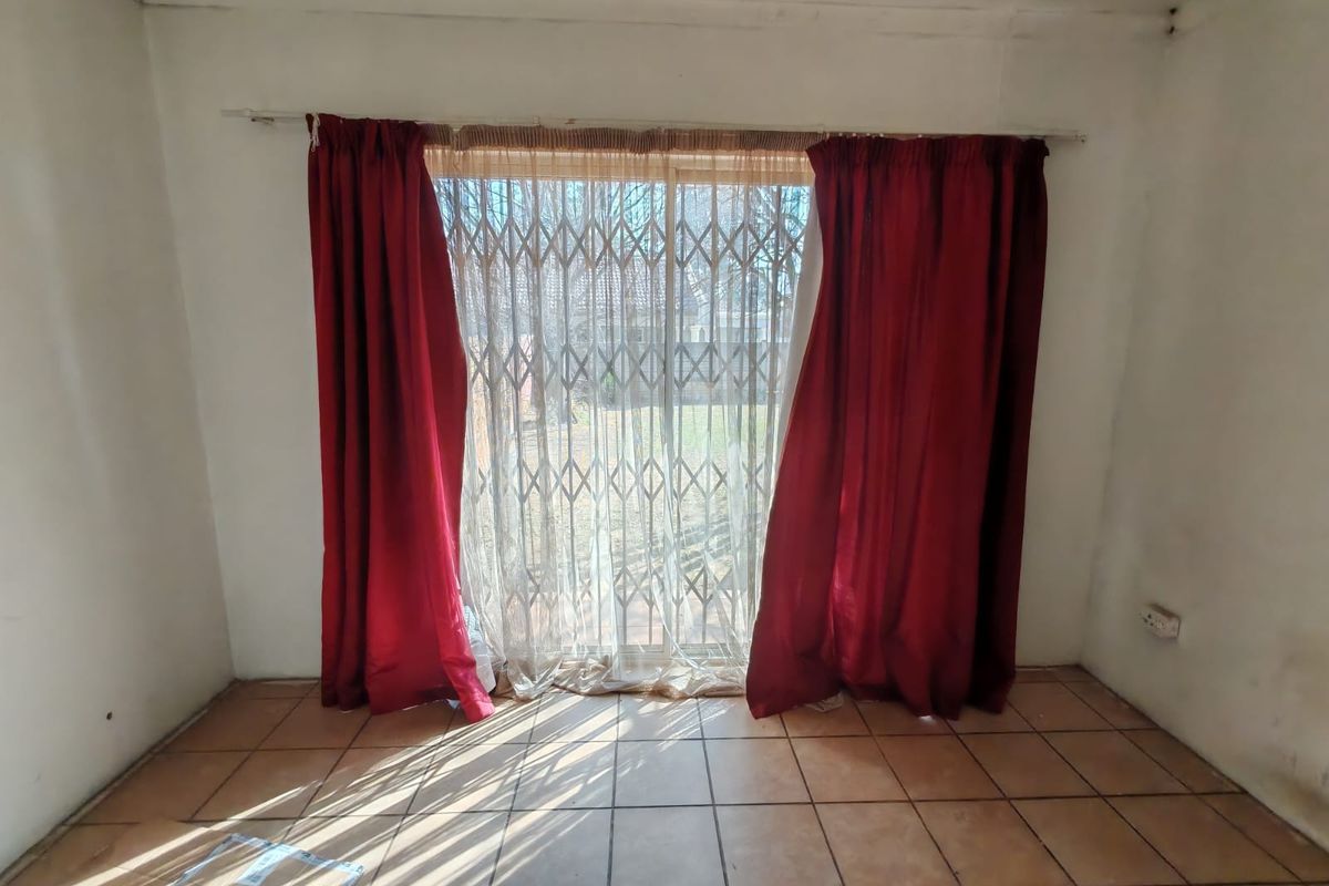 An empty living room featuring tiled flooring and a sliding glass door with a security gate, offering direct access to the outdoor area.