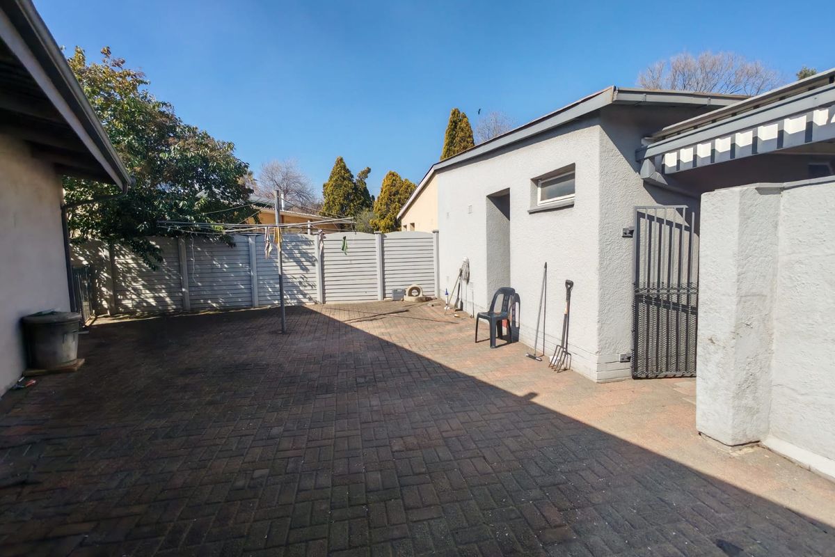 A paved rear courtyard area featuring a precast concrete boundary wall, metal security gate, and a rotary clothesline.
