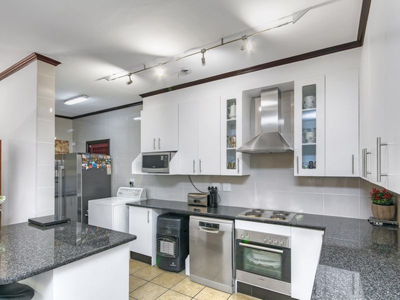 A functional kitchen featuring white cabinetry, granite countertops, a built-in oven, hob, extractor fan, and integrated space for laundry appliances.