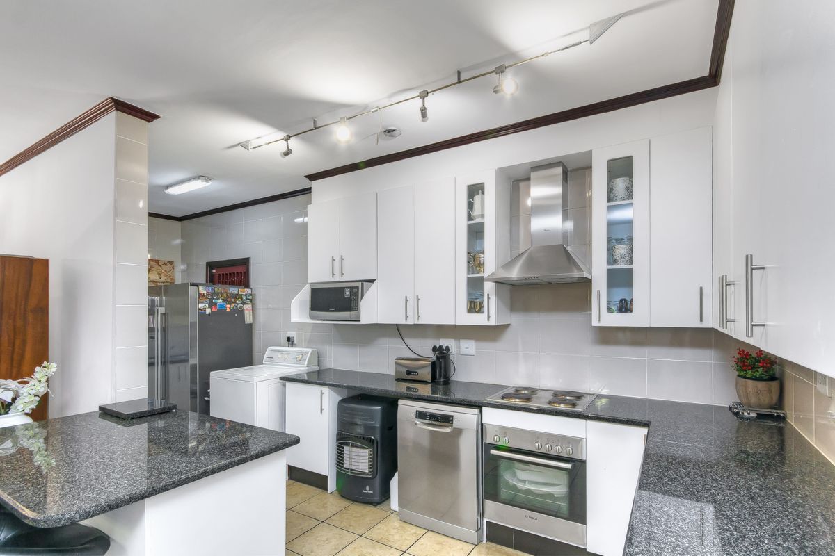 A functional kitchen featuring white cabinetry, granite countertops, a built-in oven, hob, extractor fan, and integrated space for laundry appliances.