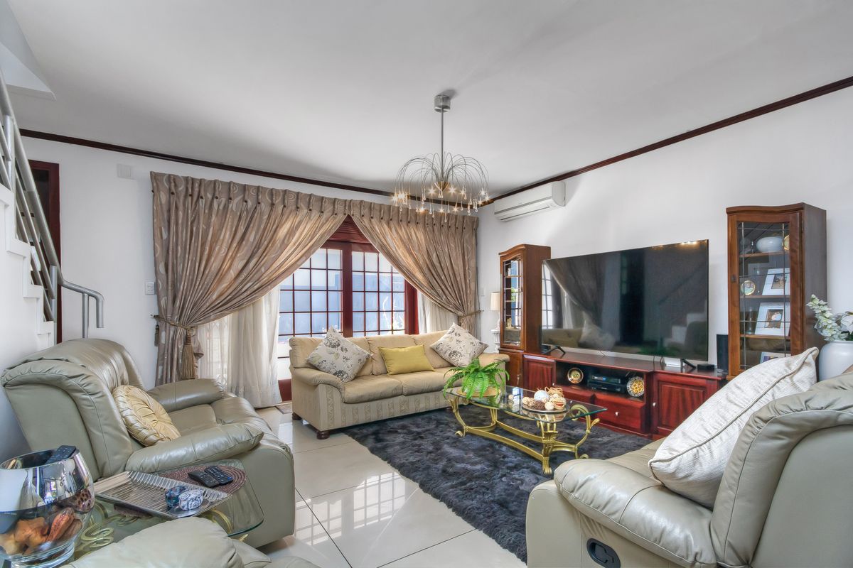 A comfortable living room featuring tiled flooring, a wall-mounted air conditioning unit, and large windows with access to the exterior.