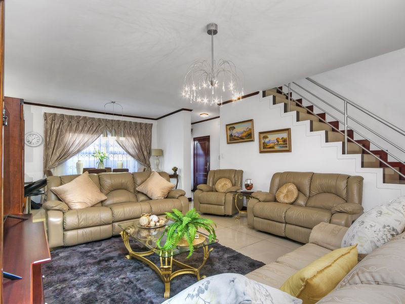Spacious open-plan living area featuring tiled flooring, a modern chandelier, and a staircase with a metal balustrade.