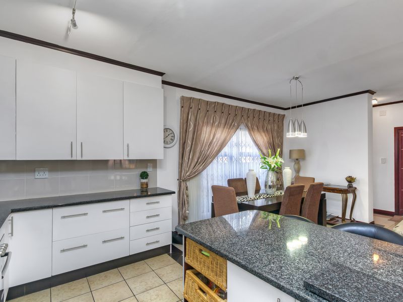 Open-plan kitchen and dining area featuring white cabinetry, granite countertops, a breakfast island, and tiled flooring.