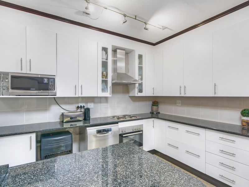 A modern kitchen featuring white cabinetry, granite countertops, a built-in oven, hob, extractor fan, and integrated microwave.