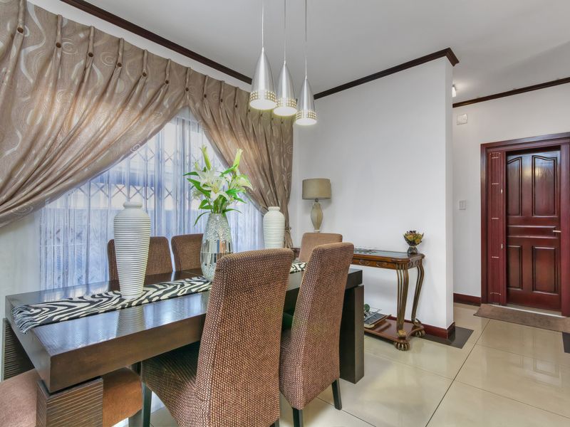 A well-maintained dining area featuring polished tile flooring, crown molding, and modern pendant lighting, leading to a solid wood entrance door.