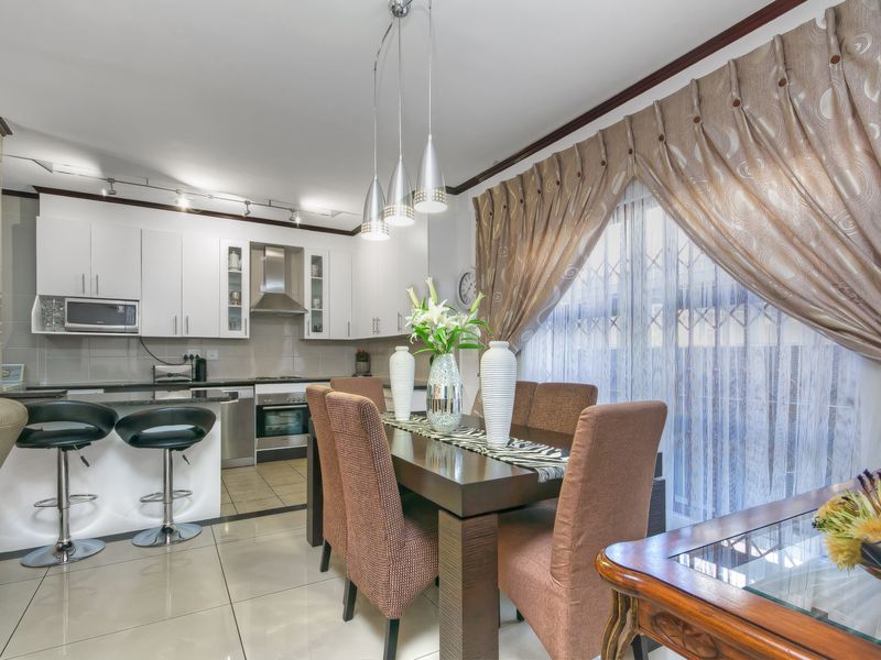 Open-plan kitchen and dining area featuring white cabinetry, granite countertops, stainless steel oven, extractor fan, and tiled flooring.