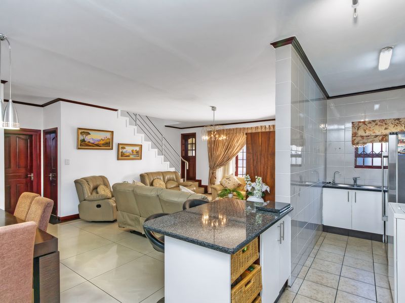 Open-plan living area featuring a kitchen with granite countertops, breakfast bar, and tiled flooring, seamlessly flowing into the adjacent dining and lounge space.