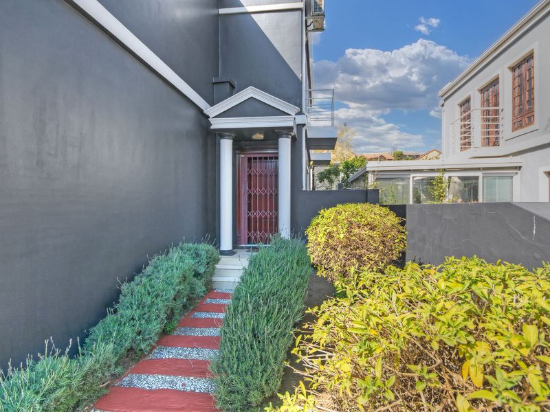 A view of the townhouse entrance featuring a paved walkway, decorative columns, and a security gate.