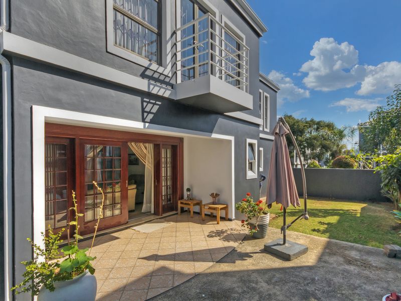 Rear view of the townhouse featuring a tiled patio, small garden area, and a private balcony accessible from the upper level.