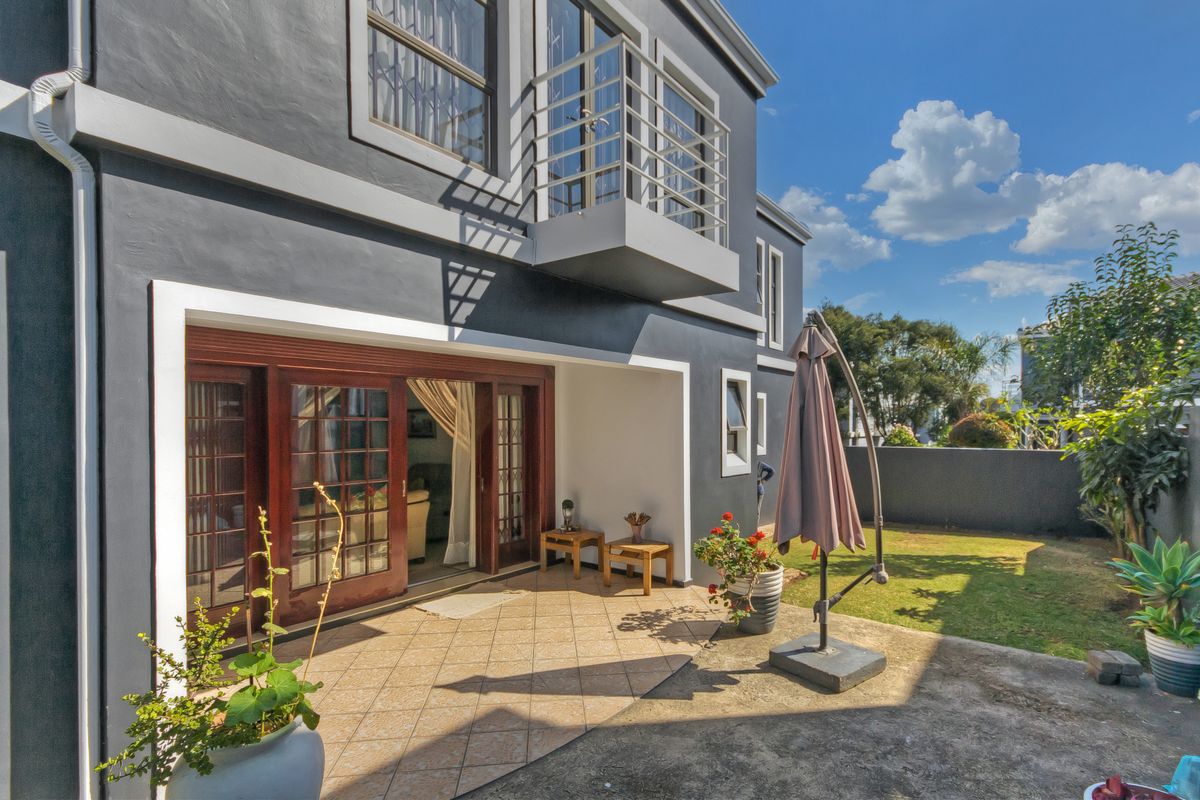 Rear view of the townhouse featuring a tiled patio, small garden area, and a private balcony accessible from the upper level.