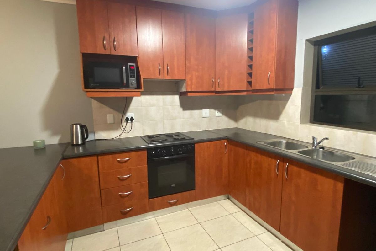 A functional kitchen featuring wood-finish cabinetry, dark laminate countertops, a built-in oven, hob, and a double bowl sink with tiled backsplash.