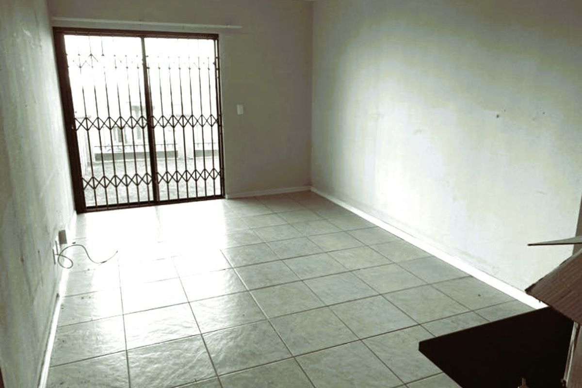 An empty living room featuring tiled flooring and a sliding glass door with a security gate, offering a blank canvas for renovation.
