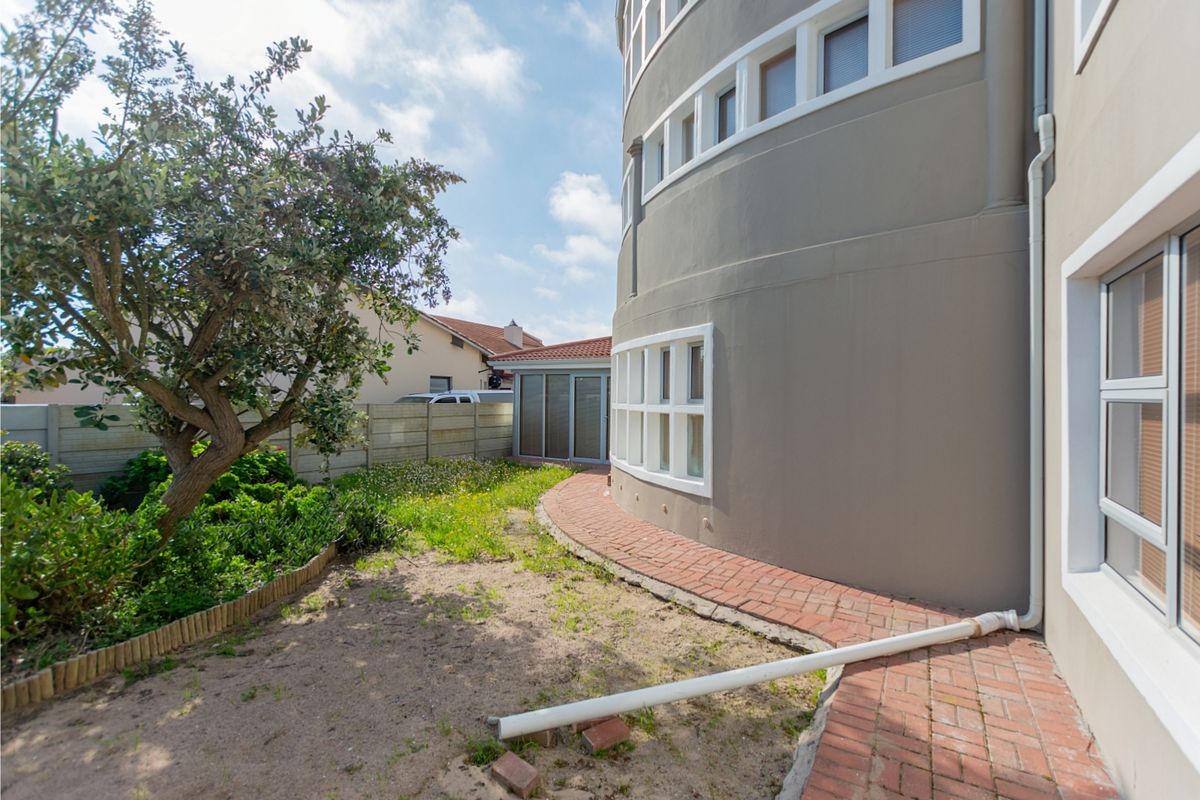 Rear exterior view of the property featuring a curved wall, brick paved walkway, and a garden area with a precast boundary wall.