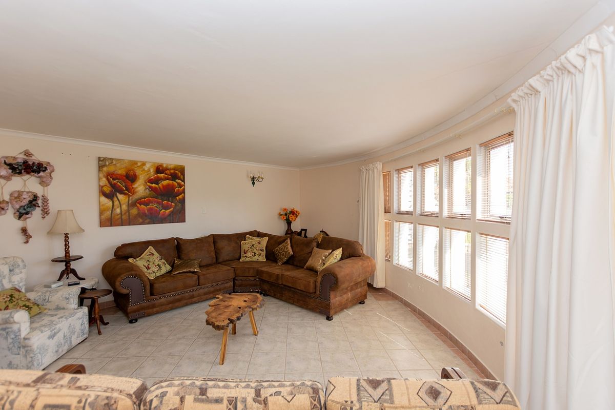 A spacious living room featuring large windows that provide ample natural light, finished with neutral tiled flooring and classic wall sconce lighting.