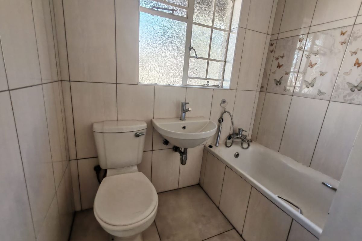 A functional bathroom featuring a bathtub, wall-mounted basin, and toilet with neutral wall and floor tiling.