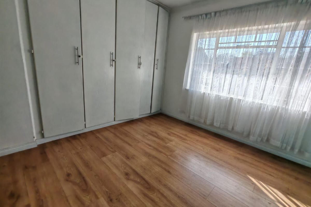A bright, empty bedroom featuring wood-look laminate flooring and extensive built-in cupboard storage space.