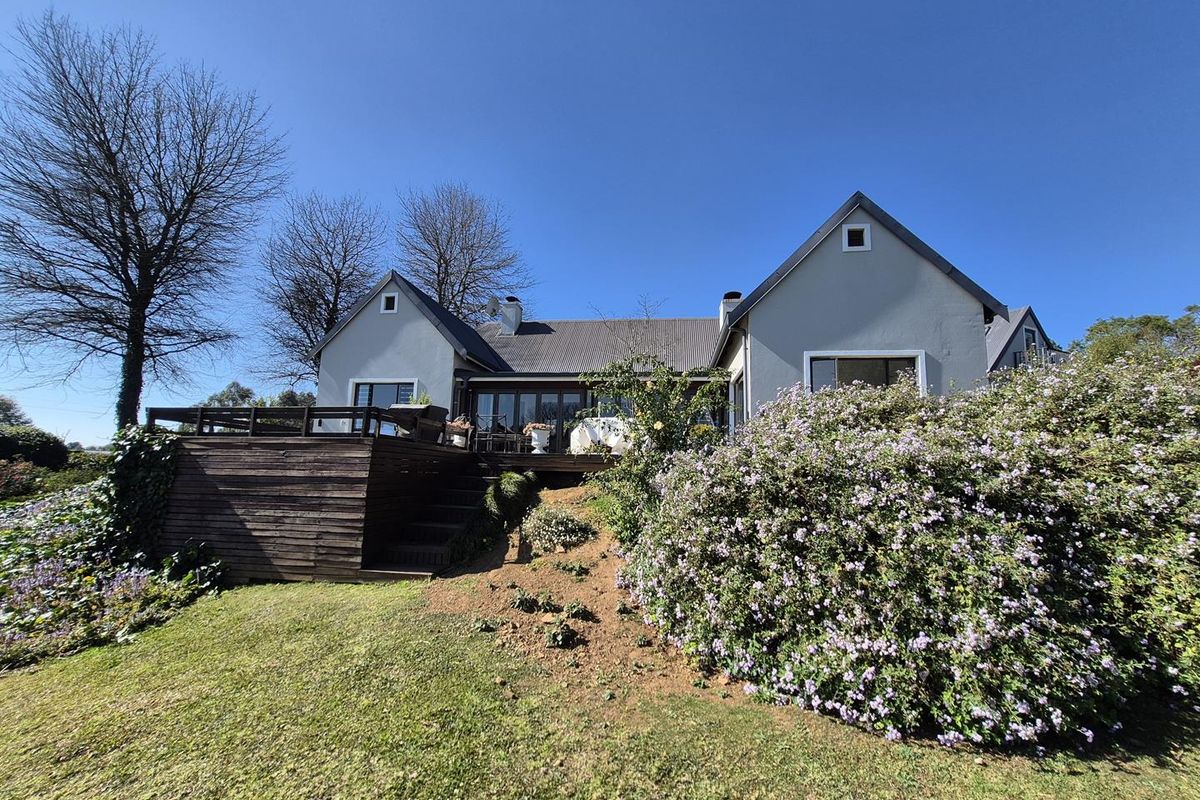 Rear view of the residence featuring a spacious timber deck, gabled roof architecture, and a well-maintained garden setting.