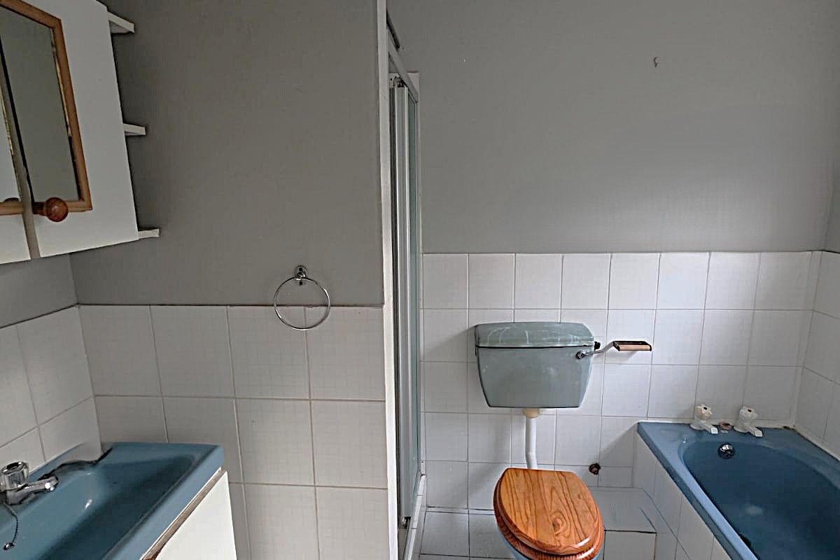 A dated bathroom featuring a blue bathtub, matching toilet, shower enclosure, and built-in vanity, requiring modernization of fixtures and finishes.