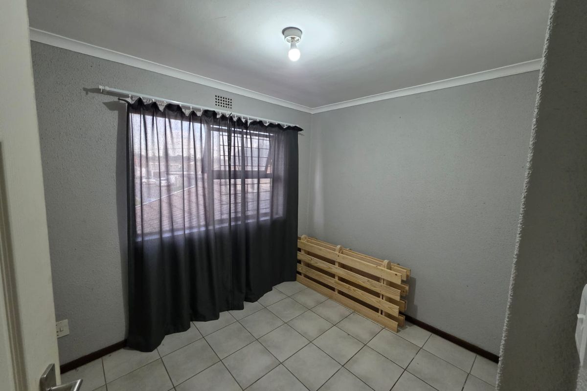 A vacant bedroom featuring neutral grey walls, tiled flooring, and a window fitted with security burglar bars.