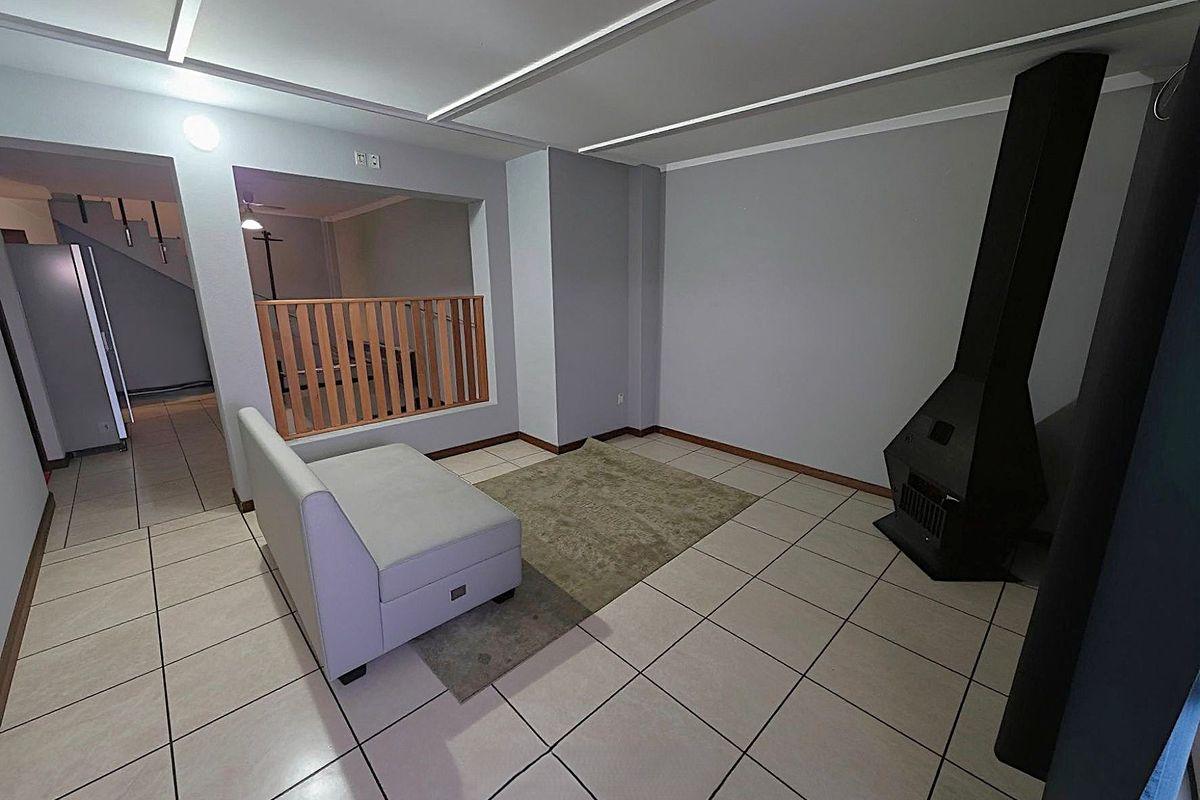 Spacious living area featuring tiled flooring, a modern freestanding fireplace, and an open-plan layout with a timber balustrade overlooking the lower level.