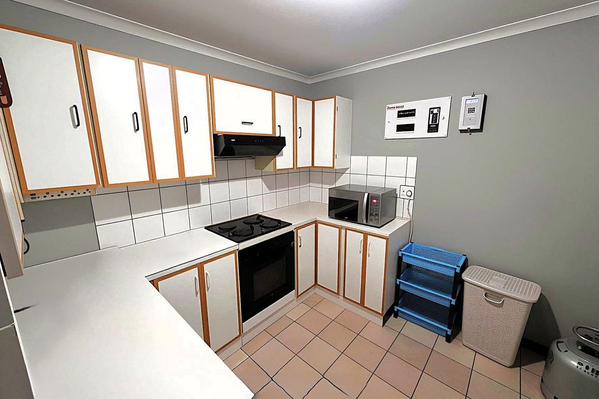 Functional kitchen featuring white cabinetry with wood trim, tiled backsplash, built-in oven, electric hob, and ceramic floor tiles.