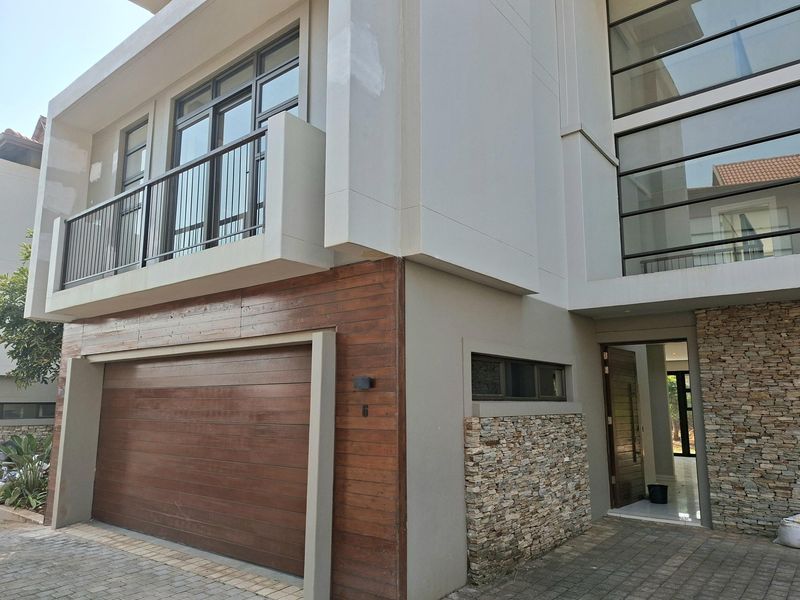 Modern multi-story residential facade featuring a timber garage door, stone cladding accents, and a private balcony with metal railings.