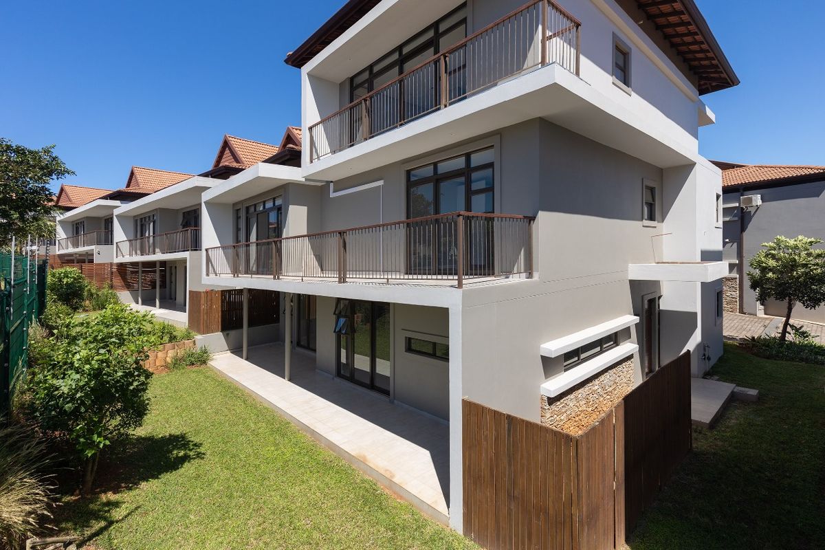 Rear view of a modern multi-story townhouse featuring stacked balconies with metal railings, a ground-floor tiled patio, and landscaped garden area.