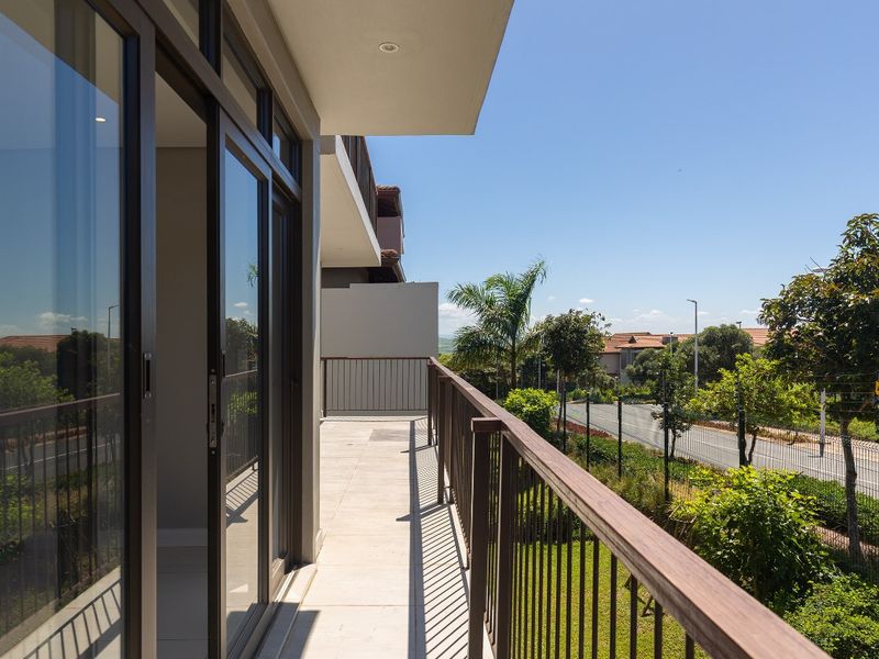 A modern, spacious balcony featuring tiled flooring, a metal balustrade, and large sliding glass doors, offering a clear view of the surrounding neighborhood.