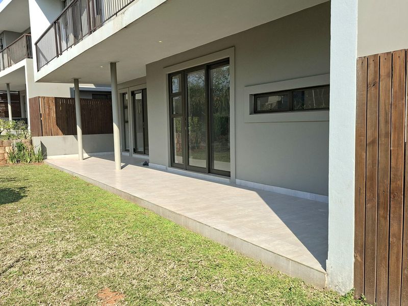 A spacious covered patio featuring tiled flooring, recessed lighting, and direct access to the garden through large sliding glass doors.