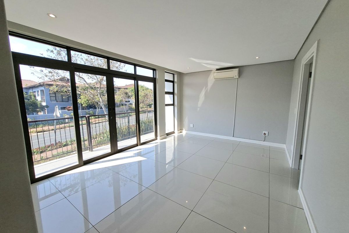A bright, empty living room featuring large format floor tiles, recessed lighting, a wall-mounted air conditioner, and expansive aluminium sliding doors leading to a balcony.