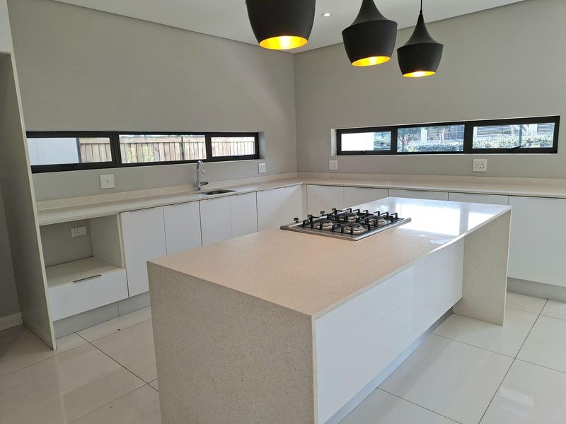 Modern kitchen featuring a central island with a gas hob, stone countertops, sleek white cabinetry, and horizontal windows providing natural light.