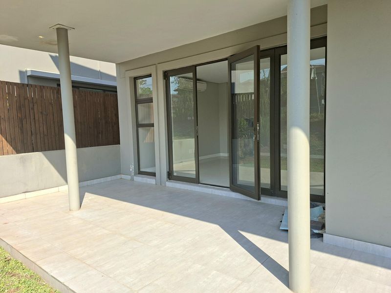 A covered patio area featuring tiled flooring, support columns, and large aluminium-framed glass doors leading into the interior living space.