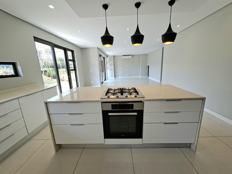 Modern open-plan kitchen and living area featuring a central island with gas hob, built-in oven, sleek cabinetry, and large sliding doors leading outdoors.
