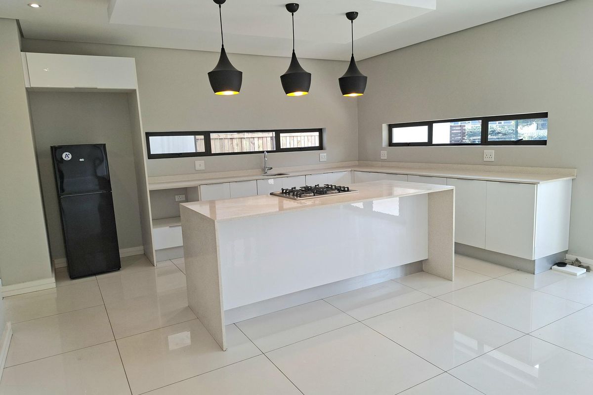 Modern kitchen featuring a central island with a gas hob, sleek white cabinetry, stone countertops, and polished tiled flooring.